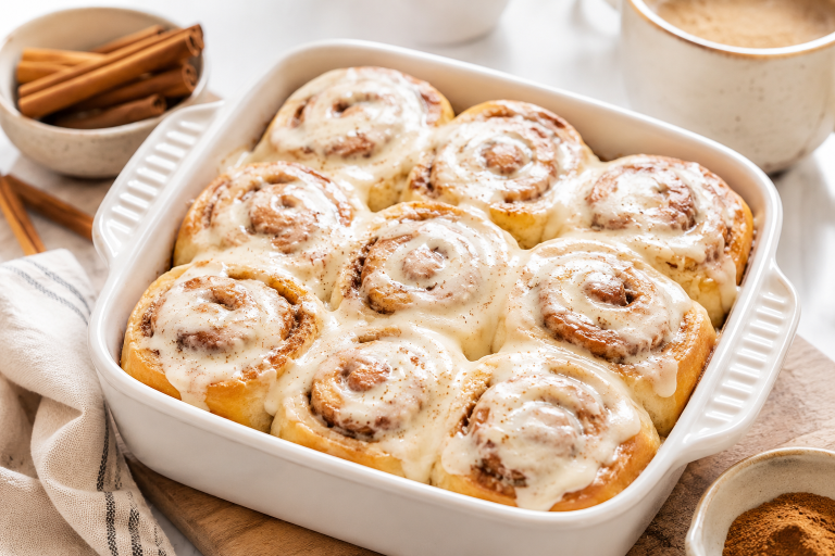Healthy high protein cinnamon rolls with cream cheese frosting served in a white ceramic baking dish, perfect for a healthy breakfast, brunch, or meal prep recipe.
